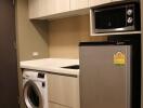 Compact kitchen with modern appliances including a refrigerator, microwave, and washing machine