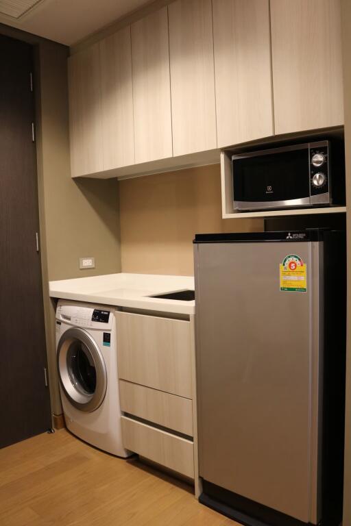 Compact kitchen with modern appliances including a refrigerator, microwave, and washing machine