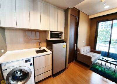 Compact and modern kitchen with integrated appliances next to a cozy living space with a comfortable sofa and natural light