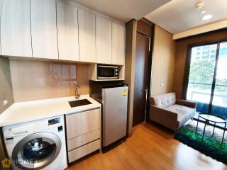 Compact and modern kitchen with integrated appliances next to a cozy living space with a comfortable sofa and natural light