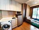 Compact and modern kitchen with integrated appliances next to a cozy living space with a comfortable sofa and natural light