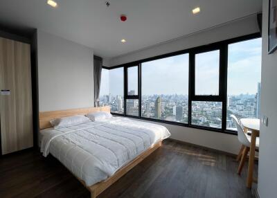 Modern bedroom with a large bed and expansive windows showcasing a city view