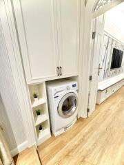 Compact utility room with a modern washing machine, white cabinetry, and green plant decor