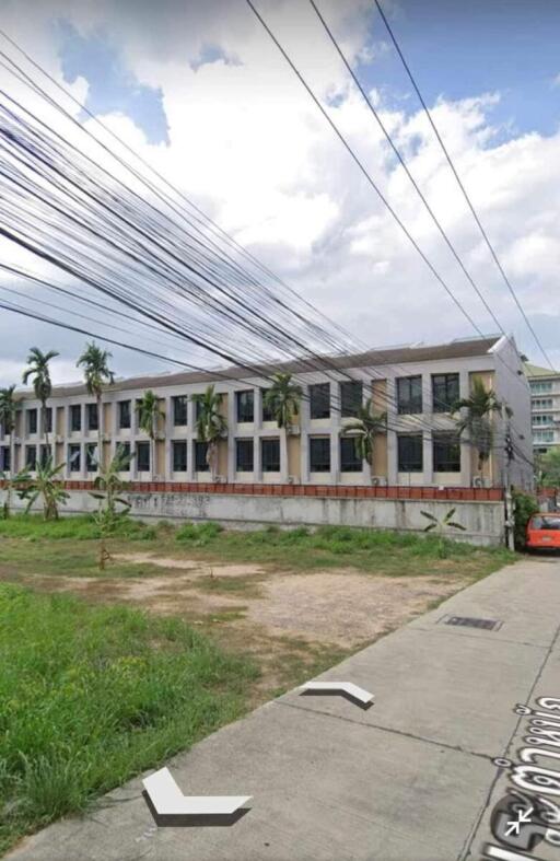 Exterior view of a two-story residential building with overgrown grass and multiple balconies under a cloudy sky