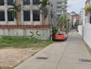 Street view of a residential building with parked car and sidewalk