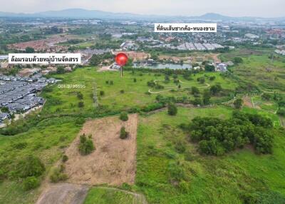 Aerial view of a vast open land with potential for development near a residential area with green surroundings