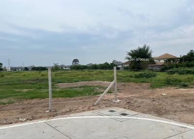 Vacant land with visible corner markers and partial pavement in front of residential area