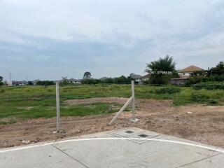 Vacant land with visible corner markers and partial pavement in front of residential area
