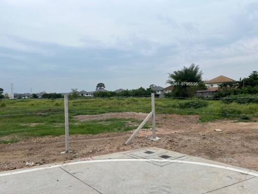 Vacant land with visible corner markers and partial pavement in front of residential area