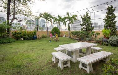 Spacious garden area with green lawn, seating arrangement, and a backdrop of an urban skyline