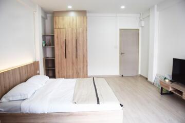 Modern bedroom interior with a large bed, wooden wardrobe, and flat-screen TV