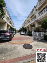 Tree-lined residential street with parked cars and townhouses