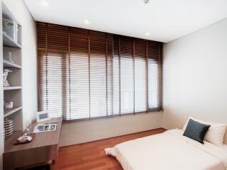 Modern bedroom interior with large window blinds, a comfortable bed, and wooden flooring