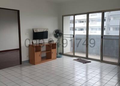Spacious and well-lit living room with tiled flooring and sliding glass door leading to a balcony