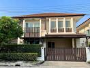 Two-story residential house with a brown gate and balcony under clear skies