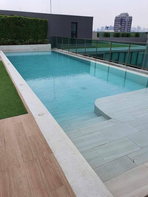 Modern outdoor swimming pool with lush greenery and urban backdrop