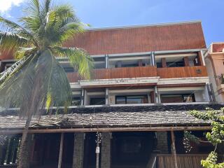 Modern multi-story residential building with a tropical aesthetic, featuring wooden elements and palm trees