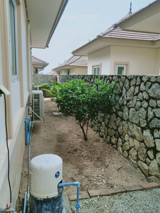 Side yard of a house with a stone wall and green plants