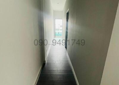 Narrow hallway with hardwood floors leading to a lit room