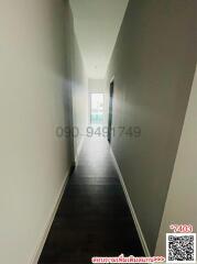 Narrow hallway with hardwood floors leading to a lit room