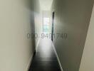 Narrow hallway with hardwood floors leading to a lit room