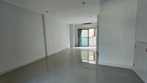 Spacious and brightly lit living room with glossy floor and glass door leading to a balcony