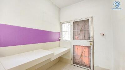 Minimalist bedroom with white walls and a bright purple accent, window with security bars, and built-in seating area