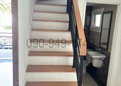 Modern staircase with wooden steps and black handrail leading to an upper floor with a glimpse of the bathroom