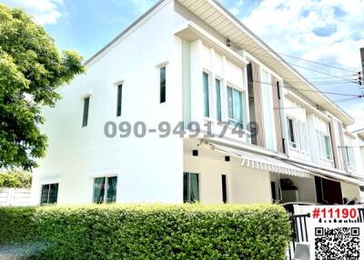 White two-story residential building with a lush green hedge and clear blue sky