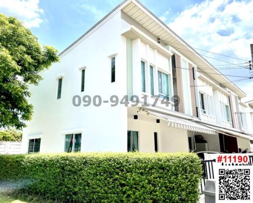 White two-story residential building with a lush green hedge and clear blue sky