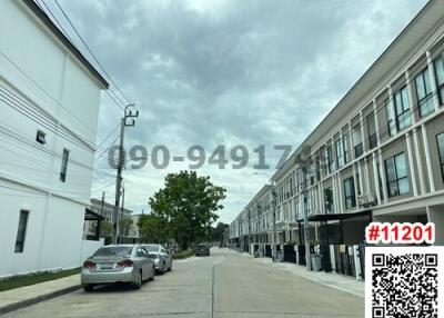 Street view of a residential townhouse complex with parked cars under cloudy sky