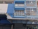 Blue multi-story residential building with balconies and shopfront