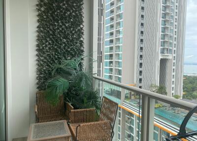 High-rise apartment balcony with ocean view, plant wall, and wicker furniture