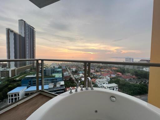 Spacious balcony with a bathtub overlooking a cityscape at sunset