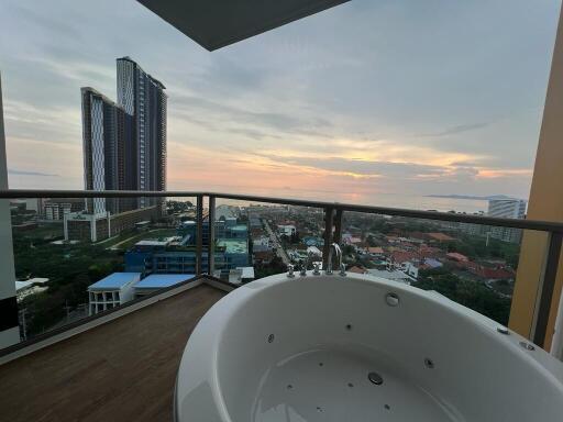 Spacious balcony with jacuzzi overlooking a cityscape at sunset