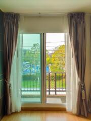 Cozy bedroom with large window and balcony access offering natural light and a view of the surroundings