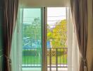 Cozy bedroom with large window and balcony access offering natural light and a view of the surroundings