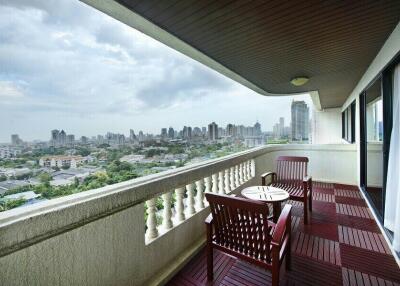 Spacious balcony with wooden flooring, outdoor furniture, and urban skyline view