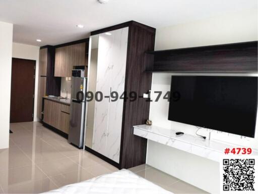 Modern apartment interior with open layout featuring a kitchen, entertainment unit, and partial view of the bedroom area