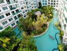 Aerial view of a residential building complex with lush greenery and a swimming pool