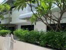 White residential building exterior with lush greenery and gated entry