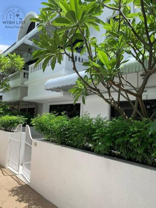 White residential building exterior with lush greenery and gated entry