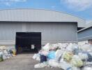 Large industrial warehouse with open bay door and surrounding waste material