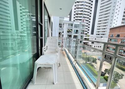 Apartment balcony overlooking a pool with modern white chair and glass safety railing