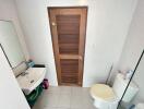 Compact bathroom with white tiles featuring a sink, toilet, and wooden door