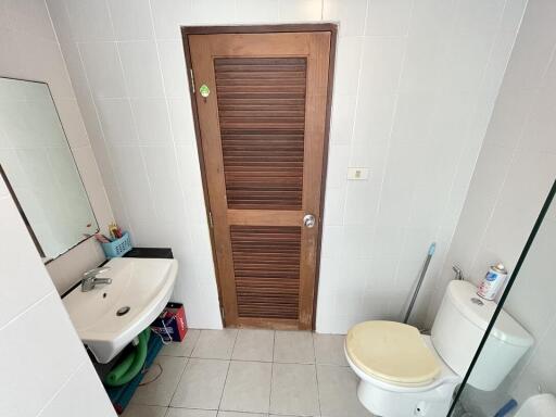 Compact bathroom with white tiles featuring a sink, toilet, and wooden door