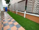 Small patio with checkered tiles and artificial grass next to a residential building