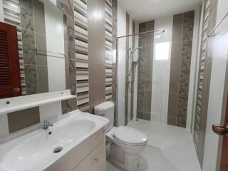 Modern bathroom with tiled walls and floor, including a shower, sink, and toilet