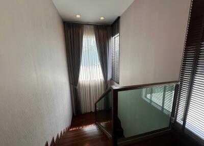 Staircase area with wooden steps and glass railing, leading to upper floor with natural light coming through the window