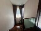 Staircase area with wooden steps and glass railing, leading to upper floor with natural light coming through the window